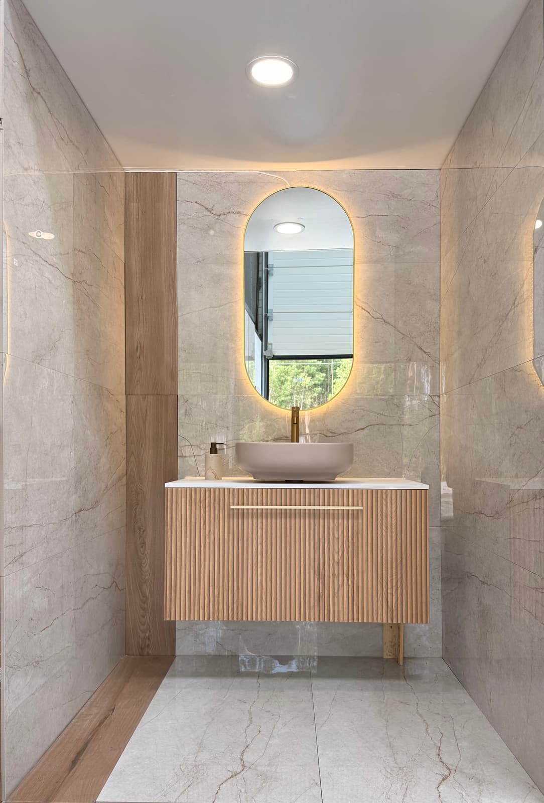 Casa de banho em showroom com móvel de madeira canelado, lavatório pousado e espelho oval com LED