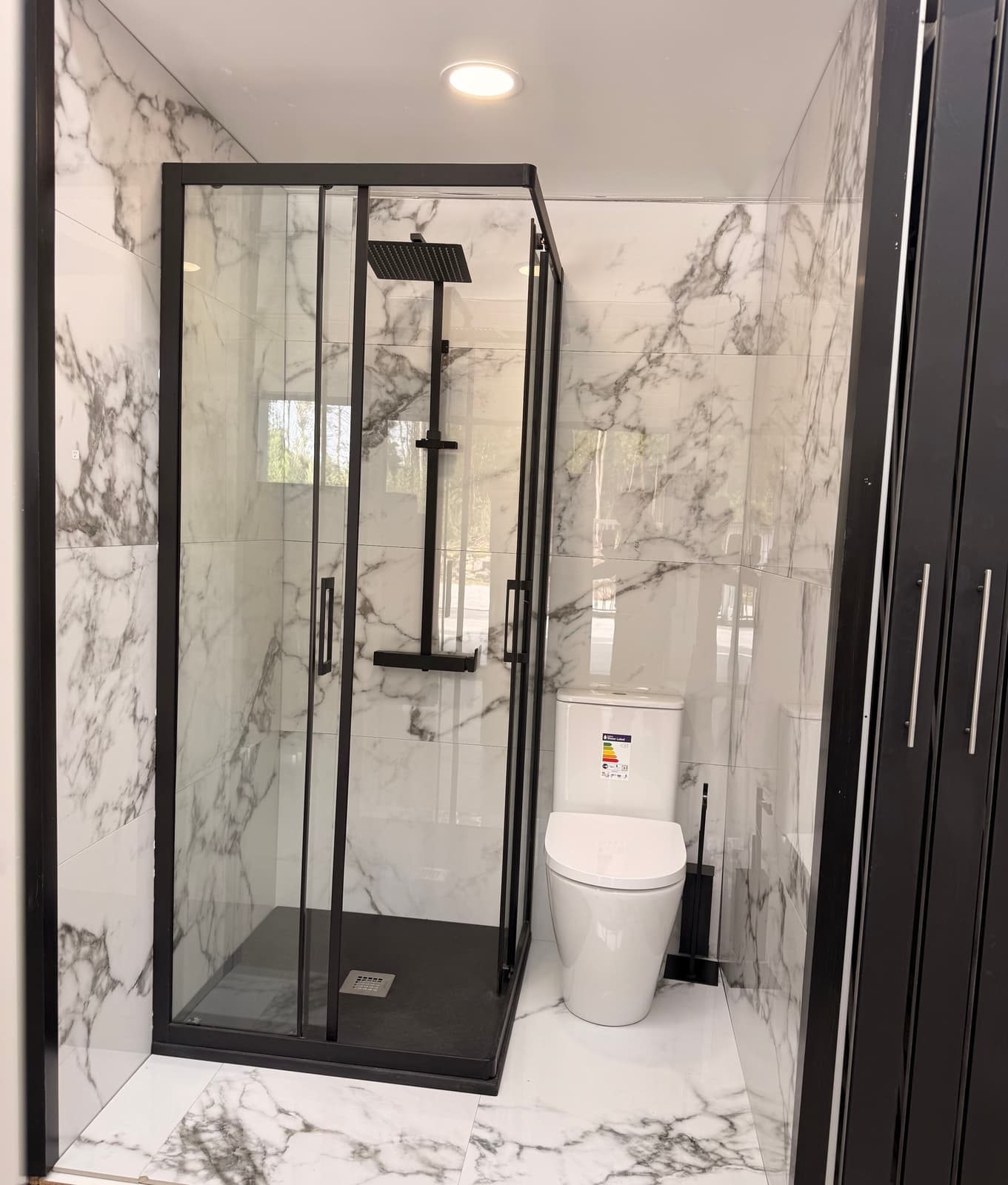Duche com resguardo em vidro e perfil preto, loiça sanitária e revestimento efeito mármore
