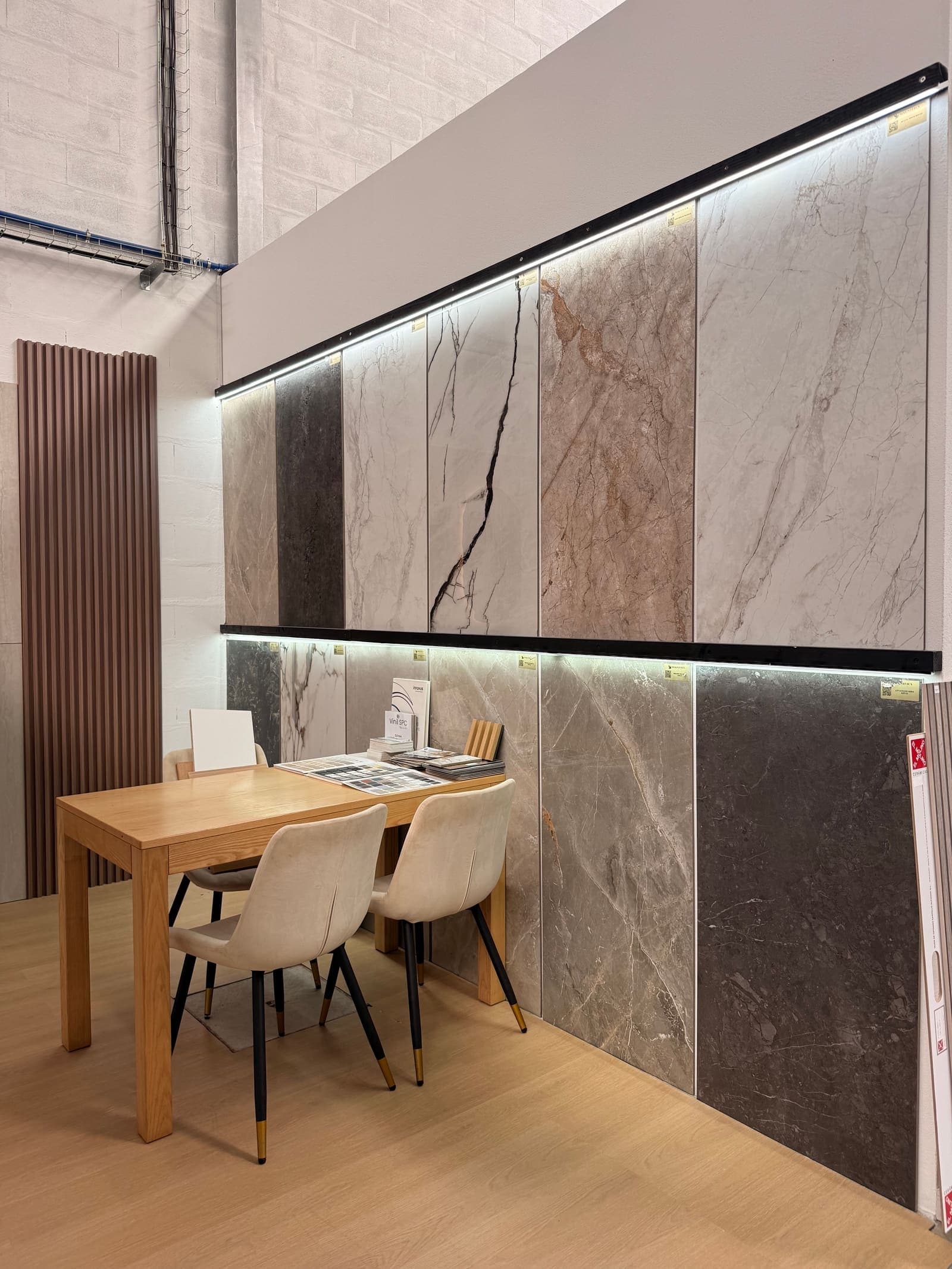 Parede iluminada de cerâmicas com mesa de consulta e cadeiras no showroom