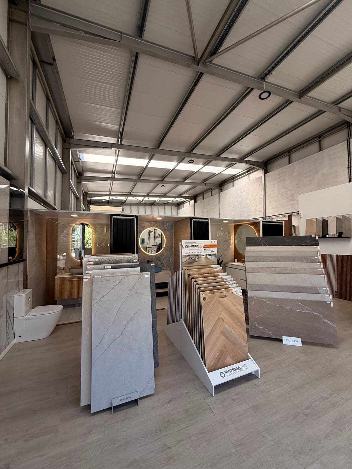 Corredor do showroom com expositores de cerâmica, pavimento SPC em espinha e pods de casa de banho